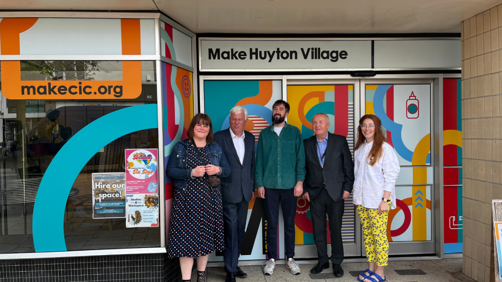 A picture of the make team standing outside of Make Huyton Village with some council members, the windows have coourful vinyl and also say 'make huyton village'